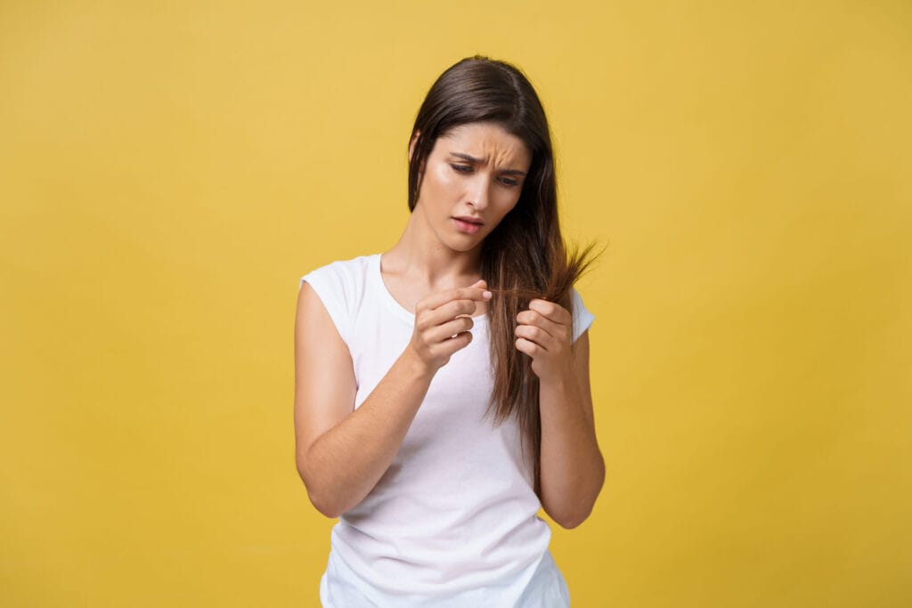 Žena drži svoju dugu kosu dok gleda oštećene i ispucale vrhove zbog problema sa negom kose.