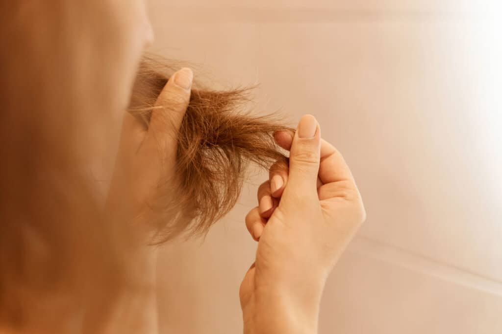 Portret ženskih ruku koje drže suvu oštećenu kosu, s problemima u vezi sa ispucalom kosom.